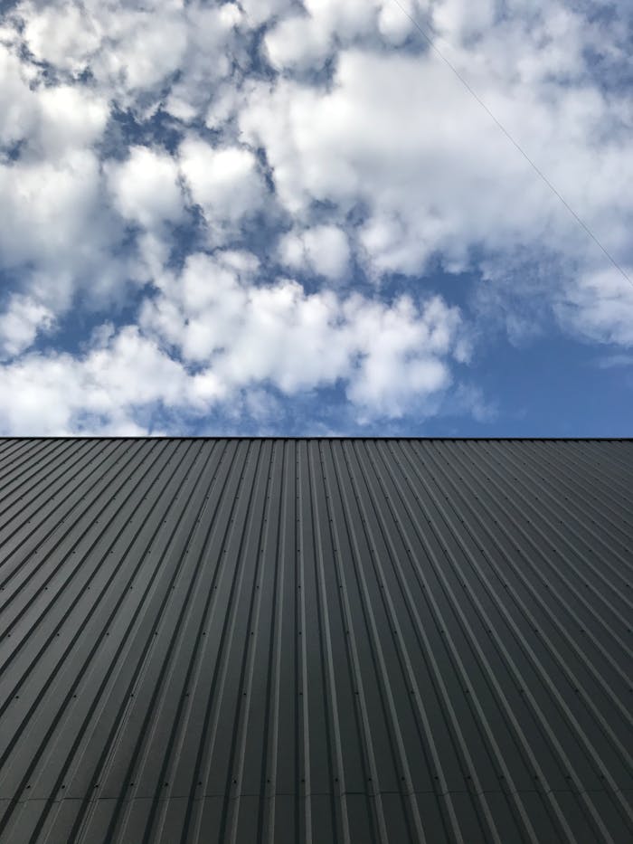 A metal roof beneath a blue sky filled with clouds, creating a stark industrial aesthetic.