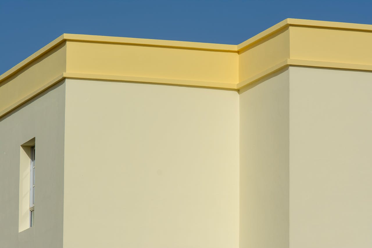 A minimalist yellow and beige building facade in bright daylight showcasing clean geometric lines.